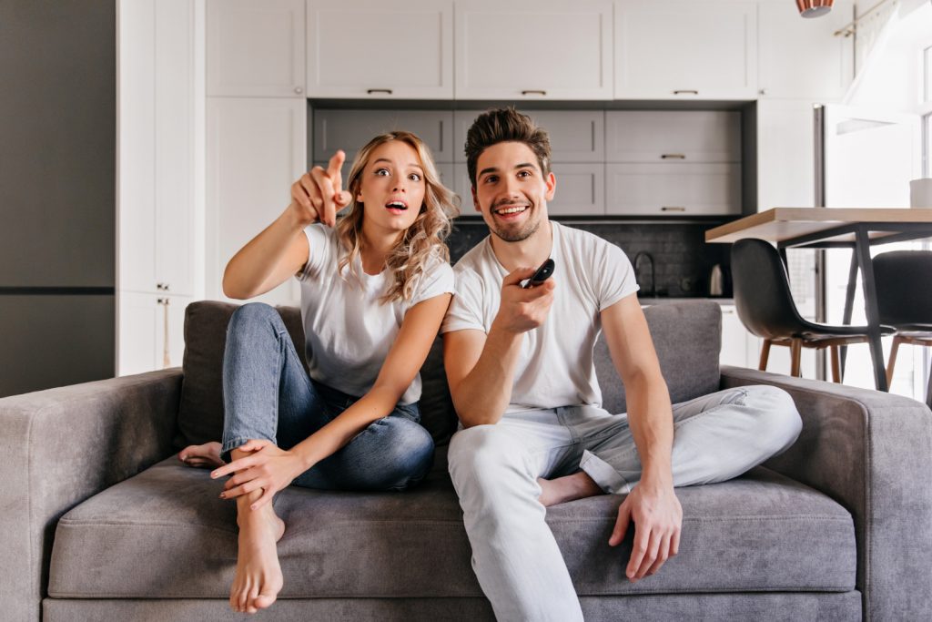 curious couple sitting on grey sofa indoor portrait of man and woman watch tv